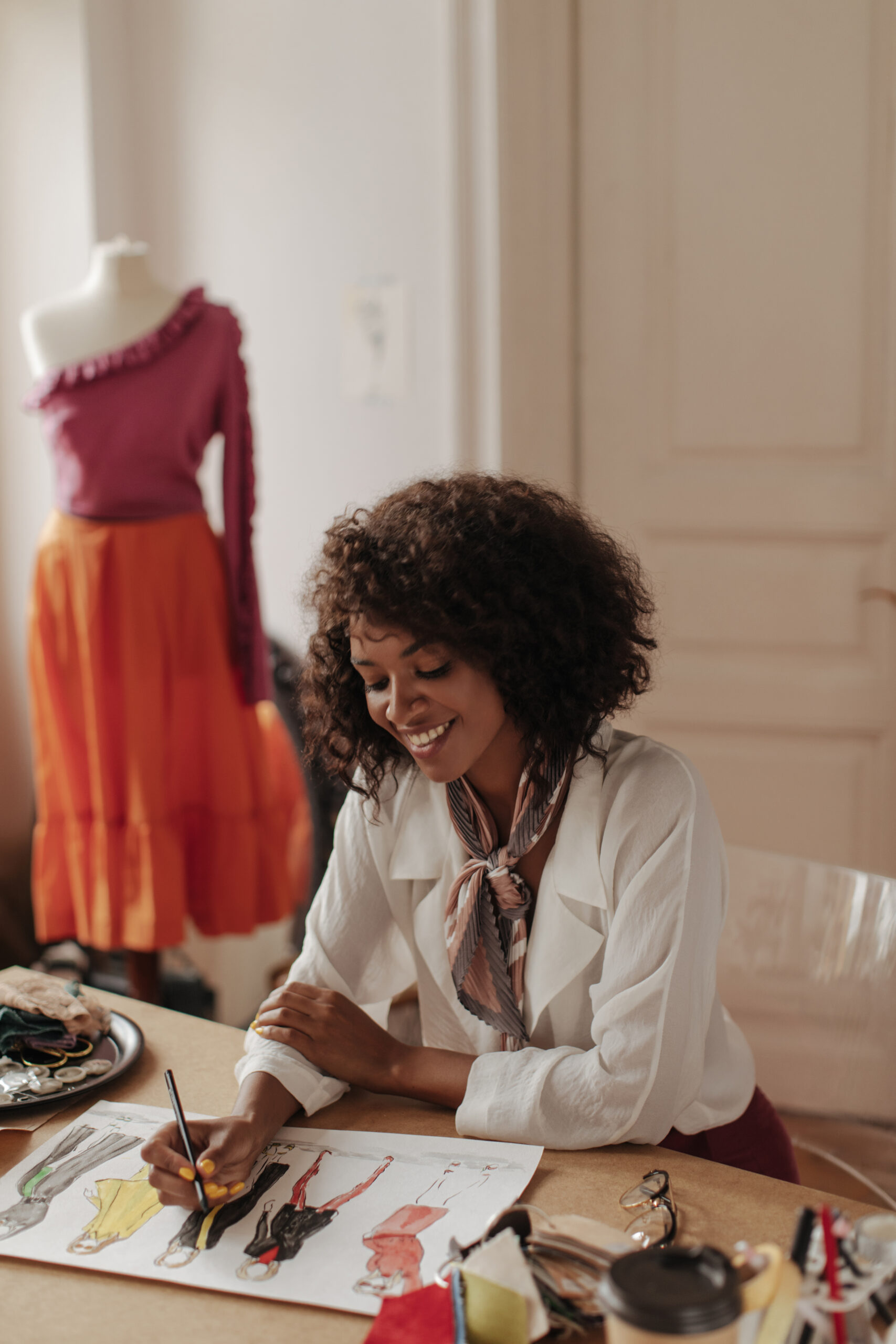 cheerful-young-darkskinned-woman-white-trendy-blouse-draws-clothes-samples-attractive-fashion-designer-sits-table-scaled.jpg